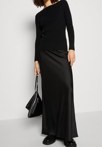 Haut noir à manches longues côtelé associé à une jupe longue en satin noire, présentant une silhouette ajustée et une texture lisse, avec un sac à main noir.