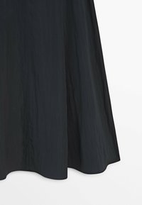 Sort krøllet stofnederdel med bløde plisseringer og udvidet kant mod en ensfarvet hvid baggrund.