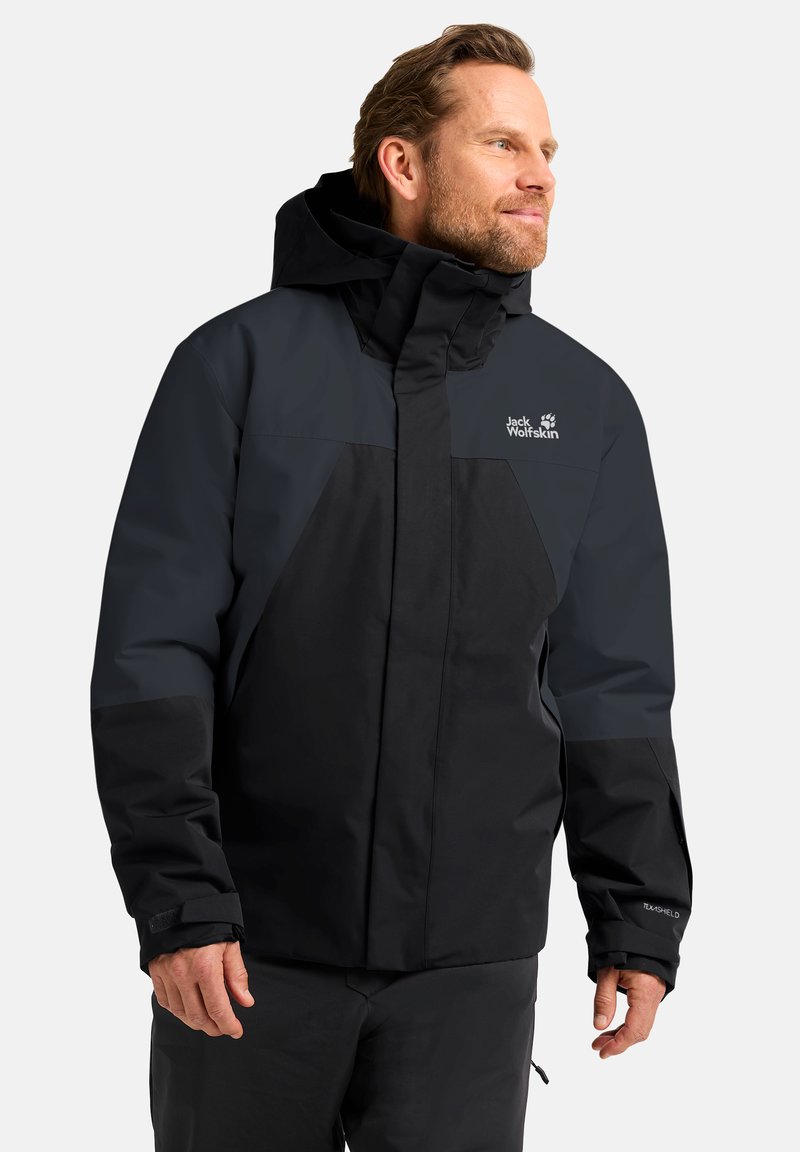 Veste imperméable noire et gris foncé avec capuche, présentant un logo, des poignets élastiques et une fermeture éclair. Convient pour les activités de plein air.