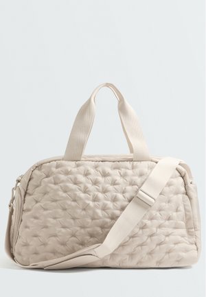 Sac de sport matelassé beige avec des poignées courtes et une bandoulière réglable sur un fond clair uni.