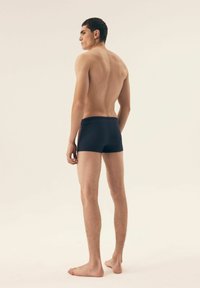 Granatowe kąpielówki, dopasowany krój, minimalne detale, gładka tekstura i długość do połowy uda. Model stoi boso, lekko obrócony na bok.
