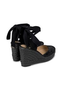 Sandales compensées noires avec une base tissée texturée, un dessus orné et des liens de cheville en tissu noir. Doublure intérieure lisse et forme de bout arrondi.