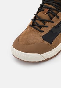 Bruna mocka- och mesh-sneakers med svarta detaljer, texturerad gummisula och kontrasterande vit mellansula; har svarta snören och sömnadsdetaljer.