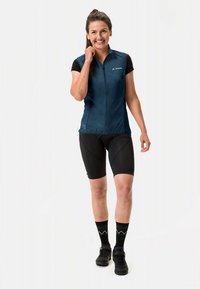 Tamsiai mėlynas dviračių liemenė su užtrauktuku priekyje, trumpomis rankovėmis, derinama su juodais dviračių šortais ir raštuotomis kojinėmis. Lengvas ir prigludęs dizainas.