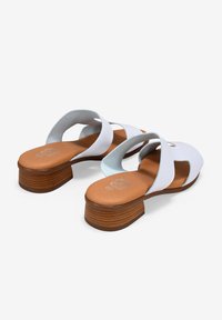 Sandalias blancas con tacón de bloque de madera, con correas cruzadas, una textura lisa y una plantilla marrón claro con la impresión de un logo.