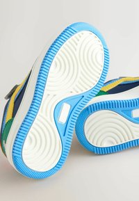 Multifarvede sneakersåler med blå og hvide gummisåler, der har teksturerede mønstre og blød indvendig polstring.