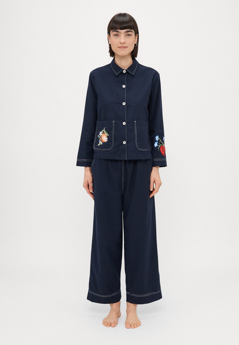 Jūras spēku divdaļīgs pidžamu komplekts ar pogājamajām augšdaļām, kurās ir izšuvumi uz kabatām, un plašām biksēm ar kontrastējošu šuvju. Mīksta auduma tekstūra.