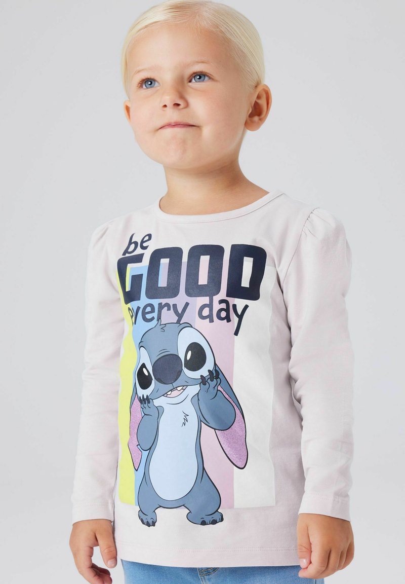 T-shirt à manches longues rose clair avec un personnage de dessin animé, accompagné du texte "be GOOD every day", et des panneaux contrastants en rose et jaune.