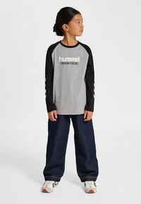 Grå långärmad T-shirt med svarta raglansärmar, med "hummel SPORTSWEAR"-logotyp. Bärs med lösa blå jeans och sneakers.