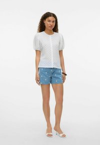 Chemisier blanc texturé avec des manches courtes bouffantes, devant à boutons ; associé à un short en jean bleu orné de motifs floraux blancs.