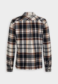 Chemise à manches longues à carreaux avec un col boutonné. La palette de couleurs comprend du bleu marine, du beige et du marron. Fabriquée en tissu doux avec une finition texturée.