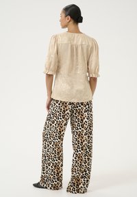 Blusa beige, testurizzata, con maniche a sbuffo abbinata a pantaloni a gamba larga con stampa leopardata. La blusa presenta un dettaglio arricciato sul retro.