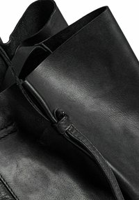 Stivali in pelle nera con una texture liscia, punta arrotondata e dettagli di cucitura sottili. Il design è minimalista senza hardware visibile.