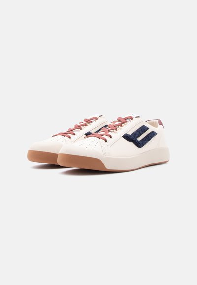 Λευκά αθλητικά παπούτσια χαμηλού ύψους με καφέ σόλες, ροζ κορδόνια και σκούρο μπλε υφασμάτινο λογότυπο στο πλάι, εμφανιζόμενα σε ανοιχτό φόντο.