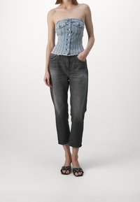 Top corsetto in denim con design senza spalline, colore blu chiaro, cuciture verticali e bottoni frontali. Abbinato a jeans cropped grigi scuri e sandali neri senza tacco.