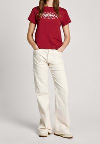 Röd bomull t-shirt med blommigt logotypdetalj på bröstet, kombinerad med off-white vida byxor och ljusa sneakers.