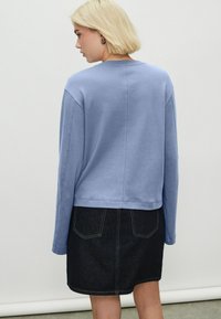 Hanorac albastru deschis cu mâneci lungi și decolteu rotund, asortat cu o fustă din denim închis, cu cusături minime și două buzunare la spate.