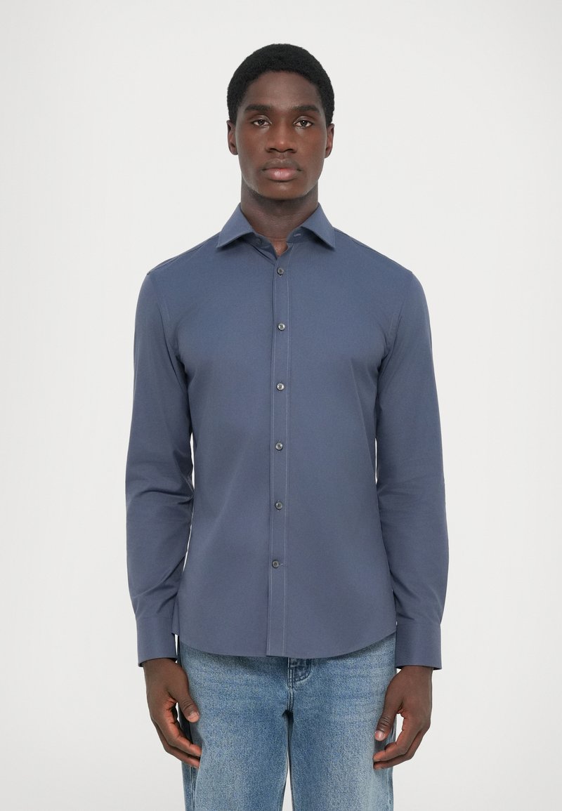Chemise à manches longues bleu marine avec un col boutonné, des boutons à l'avant et une coupe ajustée, associée à un jean bleu clair. Texture de tissu lisse.