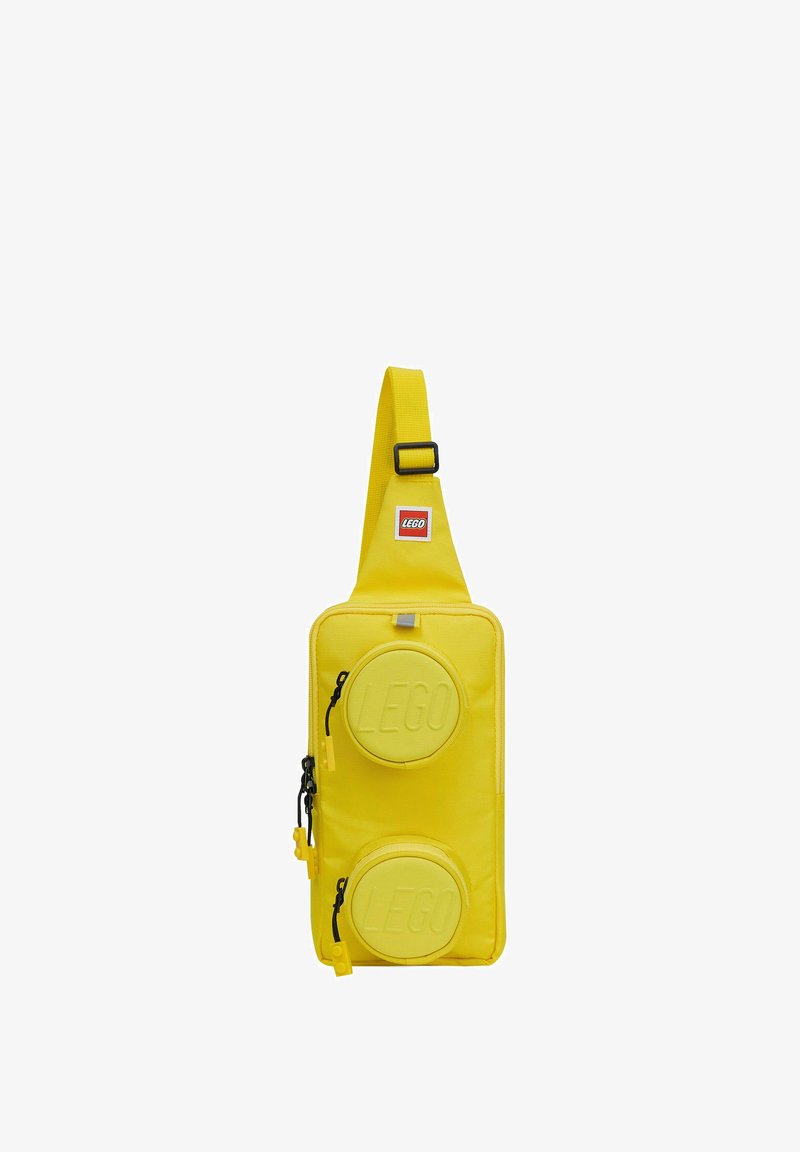 Sacoche LEGO jaune avec bandoulière ajustable et deux poches rondes zippées embossées du logo LEGO à l'avant.