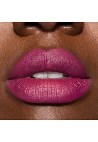 Rouge à lèvres fuchsia mat sur des lèvres pulpeuses, présentant une texture lisse et une forme définie sur une peau foncée. Dents blanches naturelles visibles.
