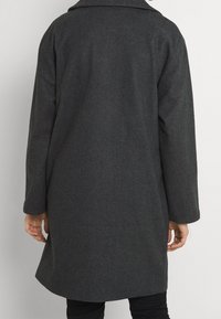 Grå herringbone-kappa med avslappnad passform, långa ärmar och notch-krage. Har en ren baksidesdesign utan synliga stängningar.