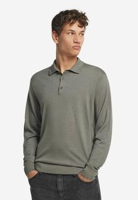Långärmad polo i dämpad olivgrön, med klassisk krage, treknappars knäppning och subtilt texturerad tyg.
