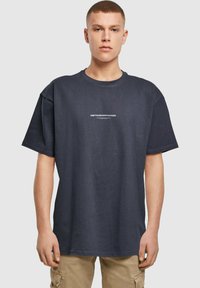 Tmavě modré oversized bavlněné tričko s bílým potiskem loga "METAMORPHOSIS" umístěným na středu hrudi. Krátké rukávy, klasický kulatý výstřih.