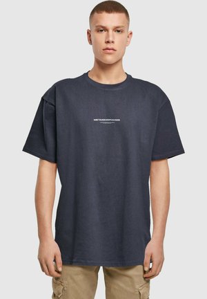 Mørkeblå oversized bomulds T-shirt med et hvidt trykt "METAMORPHOSIS" logo centreret på brystet. Korte ærmer, rund halsudskæring.