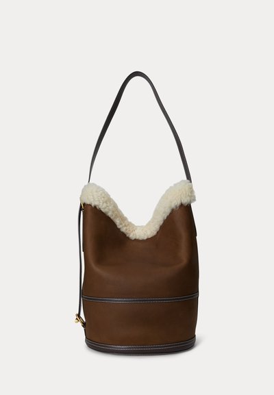 Brun skinnväska med mjuk vit fårpälskant och en enkel rem. Har en kontrasterande vit söm.