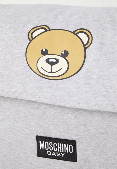 Tessuto di cotone grigio con una grafica di un volto d'orso e un'etichetta nera "MOSCHINO BABY". L'orso ha un volto beige e occhi neri.