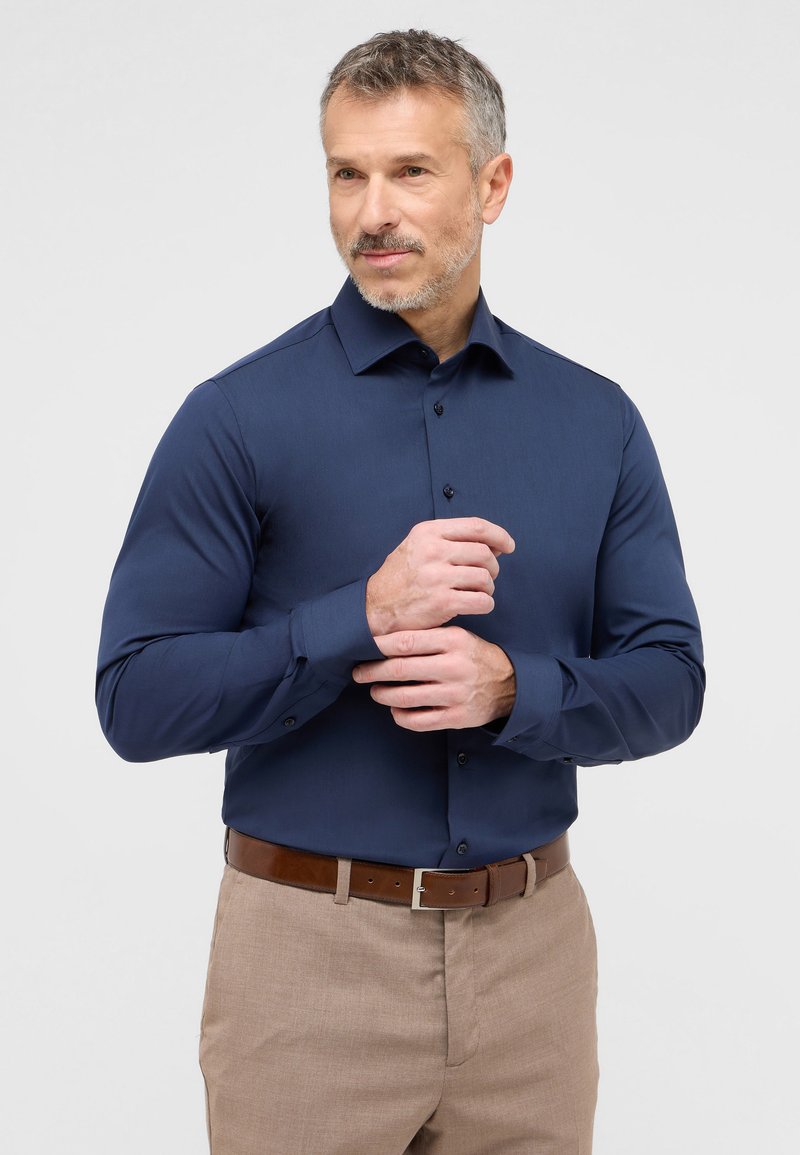 Koningsblauwe overhemden met een spread collar, lange mouwen en knopen met één knop, gecombineerd met lichtbruine broeken en een leren riem in het bruin.