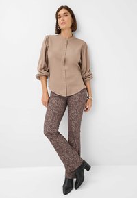 Blusa beige a maniche lunghe con chiusura a bottoni e maniche a sbuffo abbinata a pantaloni a zampa d'elefante marroni con motivo e stivali neri con tacco alla caviglia.