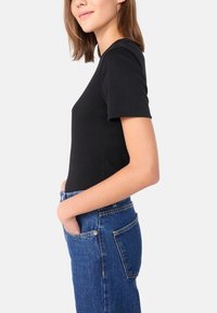 T-shirt nera a maniche corte in design aderente, abbinata a jeans blu in denim a vita alta con cuciture visibili e dettagli delle tasche.