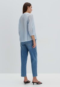 Blusa azzurra chiara, semi-trasparente, con maniche a tre quarti, abbinata a jeans in denim blu a vita alta e sandali neri con tacco.