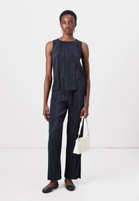 Haut sans manches bleu marine avec des plis verticaux, associé à un pantalon large assorti. Les accessoires comprennent un petit sac à main blanc et des ballerines noires.