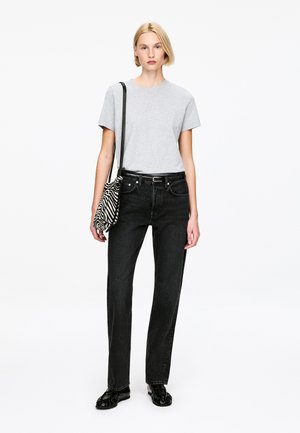 Blondynka w szarej koszulce, czarnych dżinsach z paskiem, czarnych butach, niosąca torbę na ramię w paski zebry.