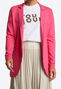 Fuchsiahäftig cardigan med lång ärm, öppen framtill och diskreta sömmar, matchad med en vit grafik t-shirt och plisserad kjol.