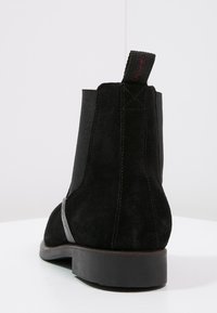 Bottine en daim noir avec panneaux latéraux élastiques, finition texturée et languette à l'arrière. Semelle plate robuste avec bord contrastant.