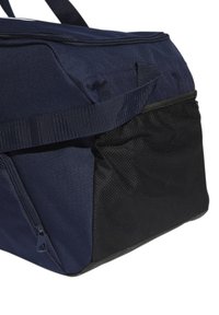 Námorně modrá cestovní taška z texturované látky, se zipovým uzávěrem a boční kapsou z černé síťoviny. Má pevné popruhy pro nošení.