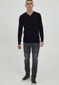 Maglione nero a scollo a V in un tessuto morbido, abbinato a jeans grigi slim-fit e sneakers nere, caratterizzato da un design semplice e una silhouette moderna.