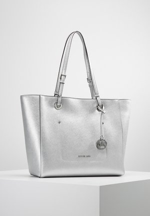 Sac cabas argenté Michael Kors avec double poignée, couture sur la poche avant, et pendentif logo métallique rond suspendu à une des poignées.