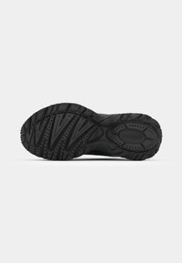 Black athletic shoe sole featuring a textured rubber design with deep grooves and ridges for traction. "LACOSTE" embossed in the center.