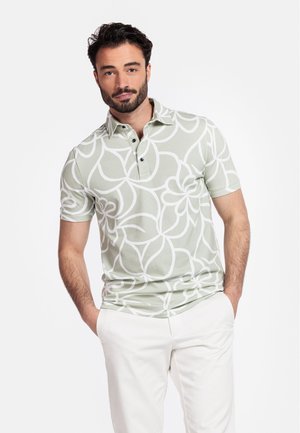 Groene polo met korte mouwen en een groot wit bloemmotief, met een kraag en een drieknoopsluiting, gemaakt van een lichte stof.