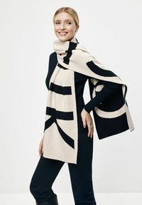 Dzianinowy szalik w kolorze kremowym i czarnym z odważnymi wzorami graficznymi. Miękka struktura w prostokątnym kształcie, elegancko układająca się wokół szyi.