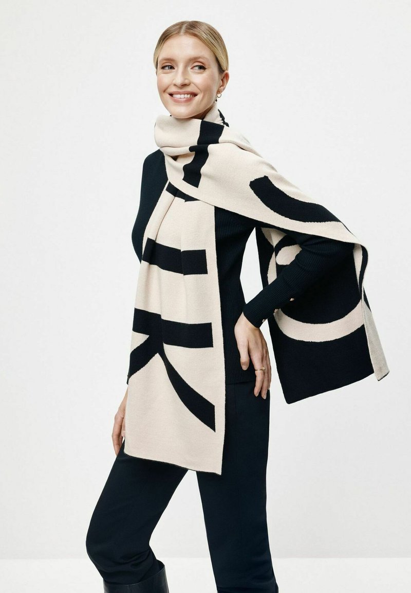 Dzianinowy szalik w kolorze kremowym i czarnym z odważnymi wzorami graficznymi. Miękka struktura w prostokątnym kształcie, elegancko układająca się wokół szyi.