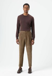 Bruine longsleeve gecombineerd met beige corduroy broek. De broek heeft een geplooide voorkant en opgerolde boorden. Bruine loafers maken de outfit af.