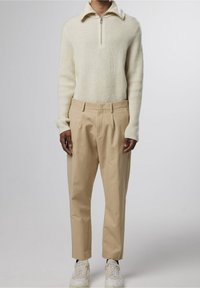 Un pull crème à côtes avec un col zippé, associé à un pantalon plissé beige clair et des baskets blanches avec des accents beige.