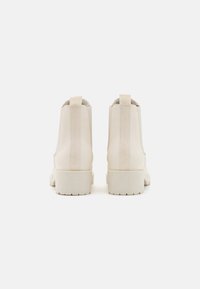 Botas de tobillo beige con un acabado de cuero suave, paneles laterales elásticos y una suela de goma blanca texturizada. Diseño minimalista, sin logotipos visibles.