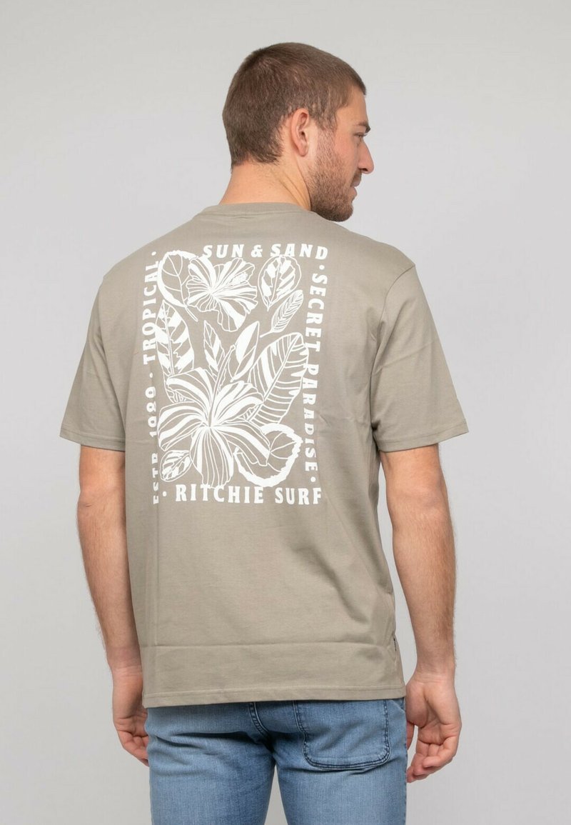 T-shirt en coton beige avec un grand graphisme de feuille tropicale blanche et du texte au dos. Manches courtes et coupe décontractée.