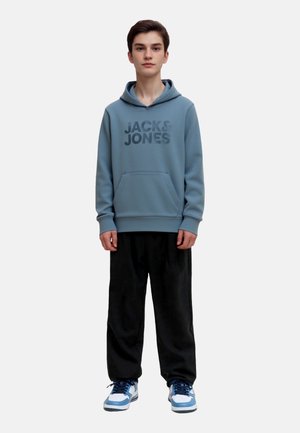 Felpa azzurra con logo "JACK&JONES", tasca a marsupio e polsini a coste in contrasto abbinata a pantaloni neri larghi e sneakers blu.